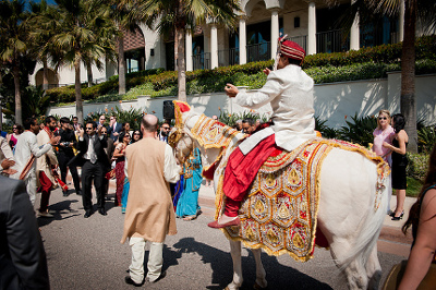 Groom riding a white horse with wedding party dancing